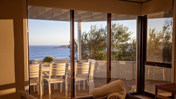 Una habitación con cama, ventana con vista al mar y zona de estar con sillas y mesa.
