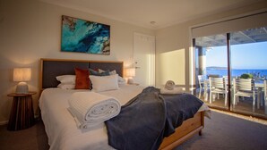 Un dormitorio con cama, un cuadro, una mesita de noche, una lámpara y vistas al mar a través de una puerta corredera.