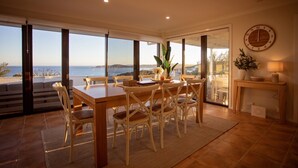 Un comedor con vistas al mar, una mesa de madera, sillas de mimbre y un reloj de pared.