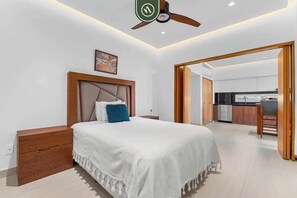 Quarto moderno com cama grande, mesas de cabeceira de madeira, ventilador de teto e vista para a cozinha.
