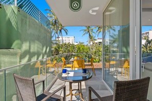 Varanda com cadeiras de vime, uma mesa de vidro e cadeiras amarelas.