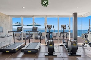 Ein Fitnessraum mit Laufbändern, Crosstrainern und Rudergerät, mit Blick auf eine schöne Aussicht.