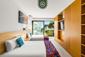 A modern hotel room with a large bed, a bedside table, a TV, and a view of palm trees through the window. - Oceanview 1 BR Condo With Private Beach - Pools (Nuevo Nayarit)