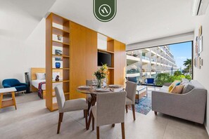 Habitación de hotel moderna con zona de comedor, sofá y vistas al exterior del edificio.