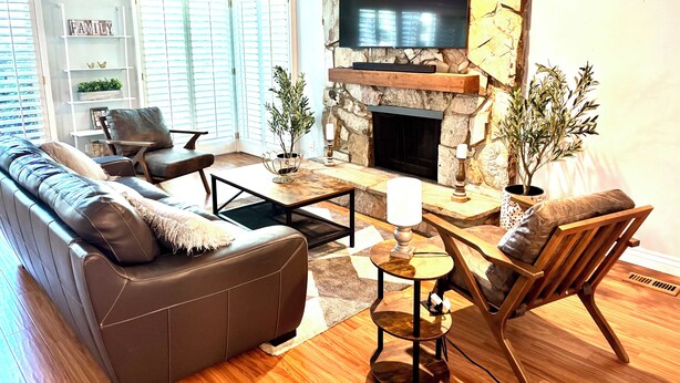 Un salon avec une cheminée en pierre, un téléviseur à écran plat, un canapé en cuir et une table basse en bois.