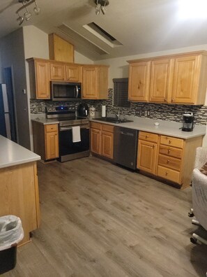 A kitchen with wooden cabinets, a microwave, stove, dishwasher, and a tiled backsplash. - Cozy 2-Bedroom House in Yuma, Arizona in a 55+ Resort Community w/Every Amenity (Yuma)