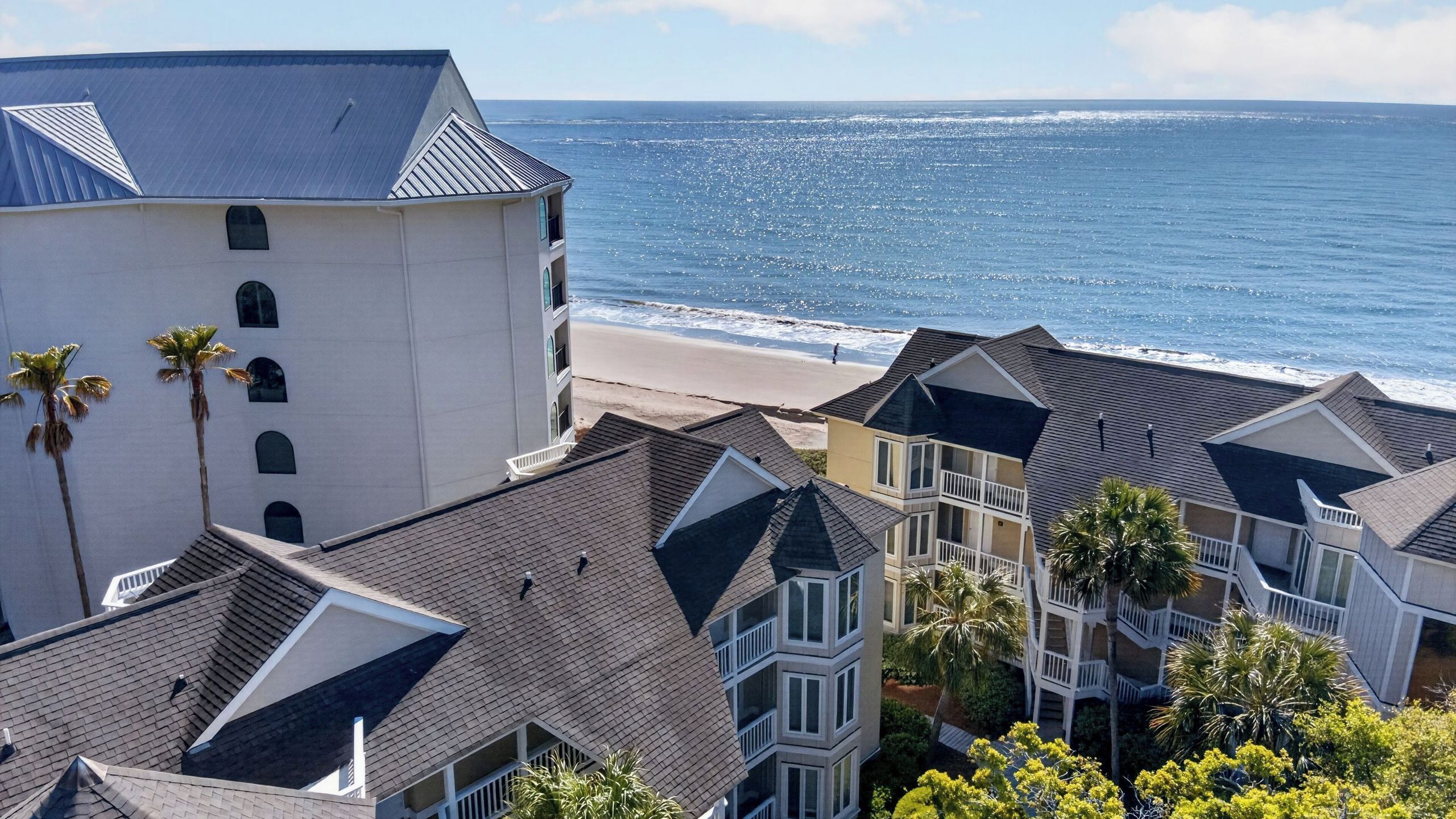 Un hôtel situé sur la côte, composé de plusieurs bâtiments, offrant une vue sur la plage et bordé de palmiers.