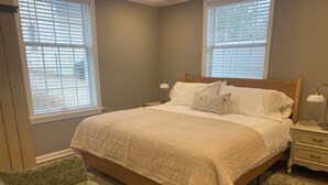 A bedroom with a bed, two bedside tables, a nightstand, a green patterned chair, and a patterned rug. - The Nook on Main St. (Hudson)