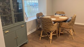 A dining area with a round table, wicker chairs, and a green cabinet with glass doors. - The Nook on Main St. (Hudson)