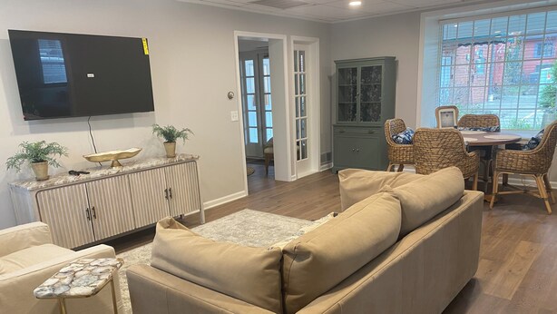 A living room with a sofa, a TV, a cabinet, and a dining area with wicker chairs. - The Nook on Main St. (Hudson)