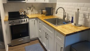 A modern kitchen with stainless steel appliances, a wooden countertop, white cabinets, and a built-in microwave. - The Nook on Main St. (Hudson)