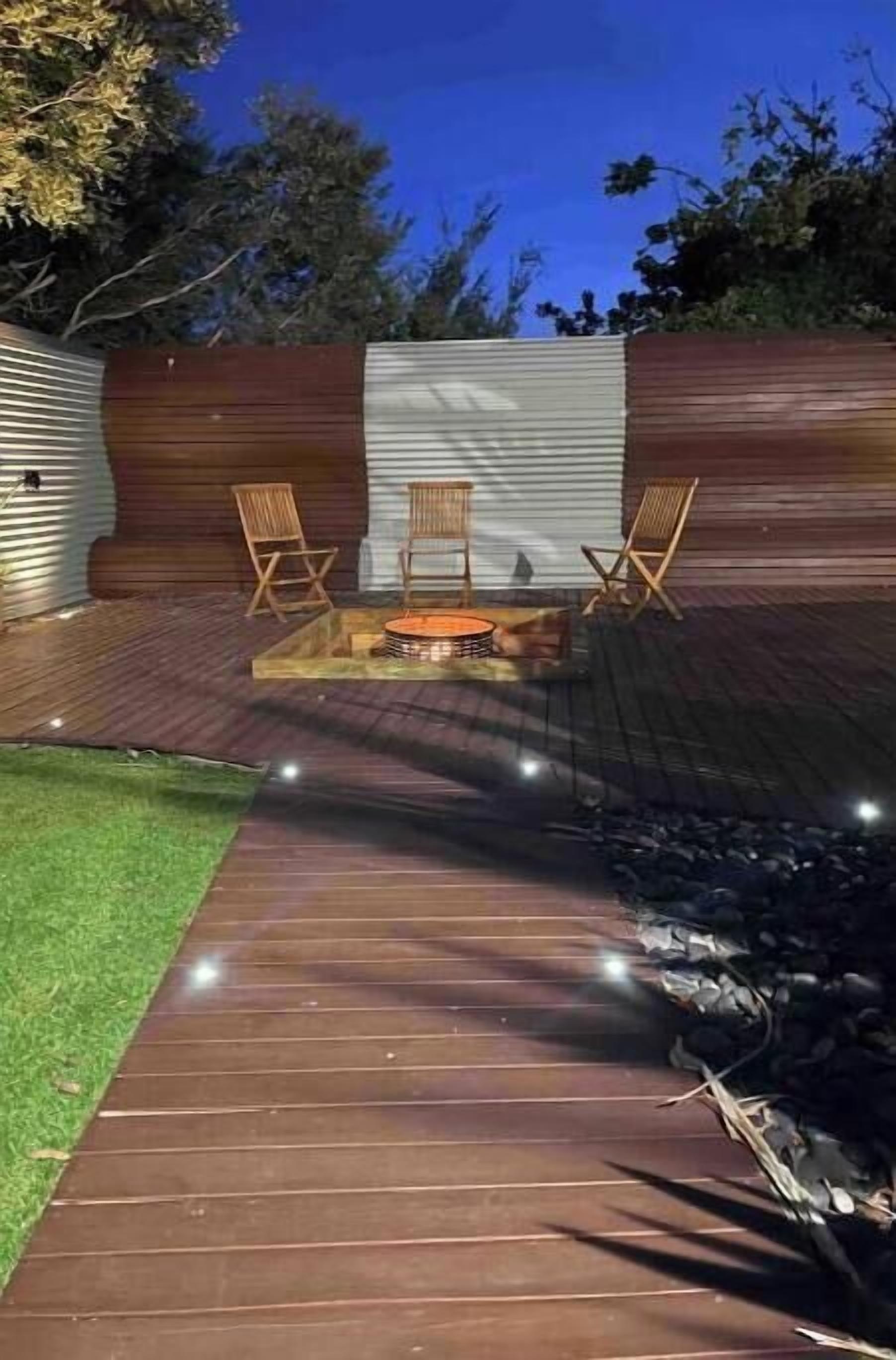 Un patio con piso de madera, un pequeño hogar y dos sillas de madera.