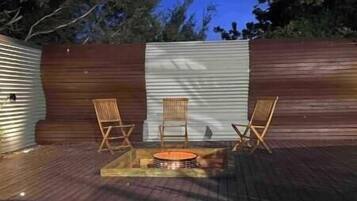 Un patio con piso de madera, un pequeño hogar y dos sillas de madera.
