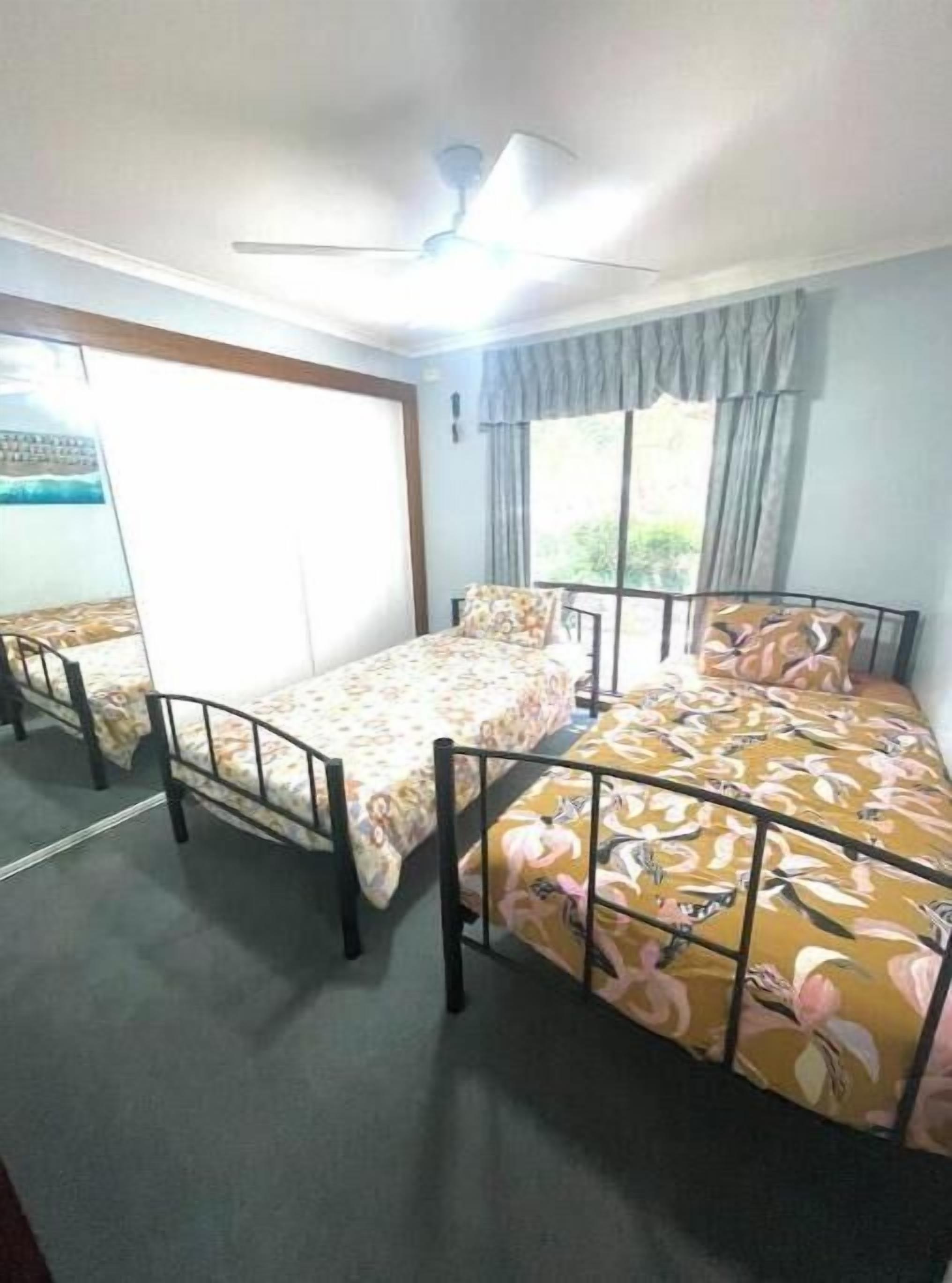 A dormitory room with two single beds, a ceiling fan, and a window with curtains.