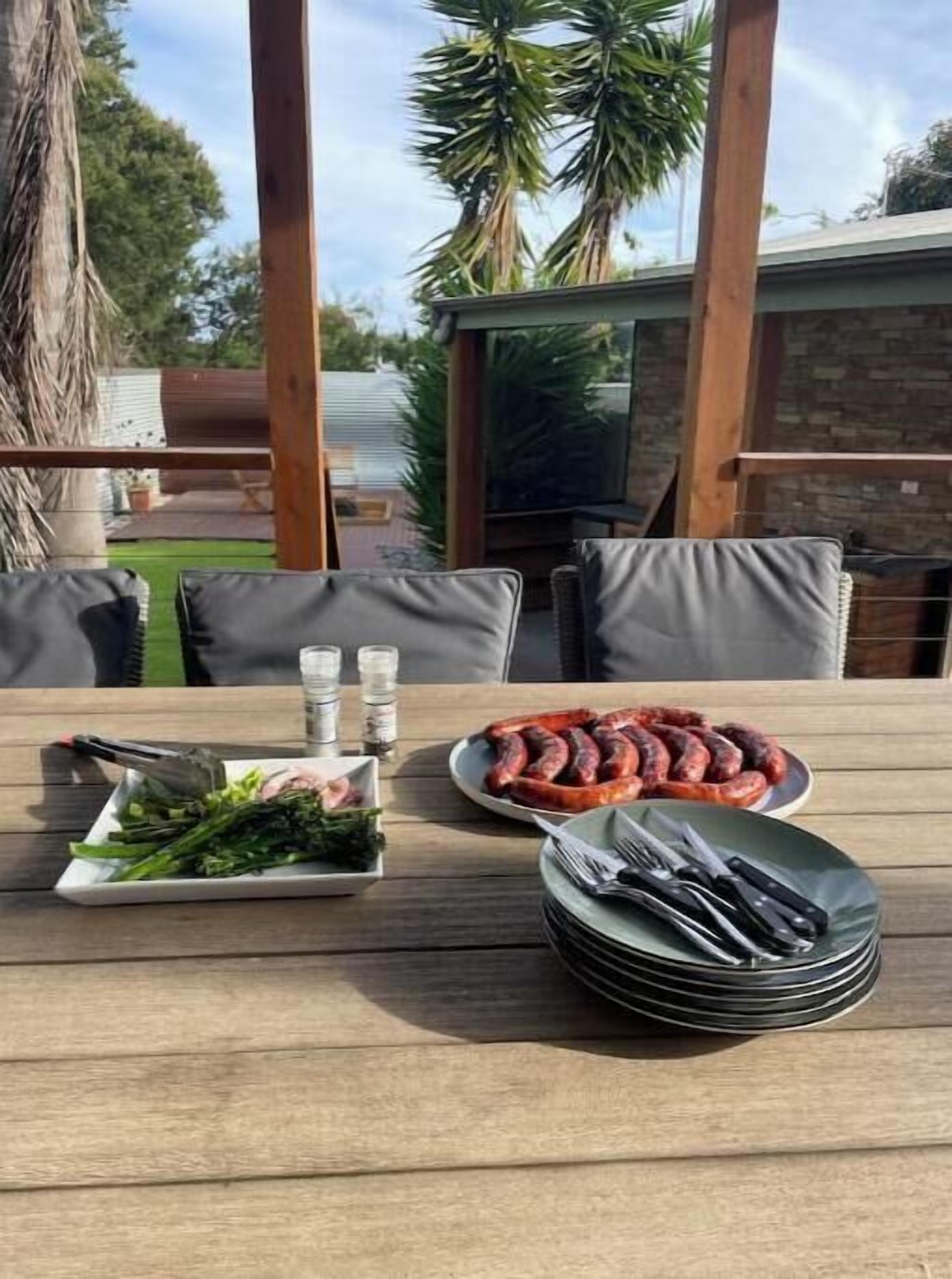 Zona d'exterior per dinar amb taula preparada per a dues persones, que inclou un plat de botifabes, un plat de verdures i una pila de coberts.