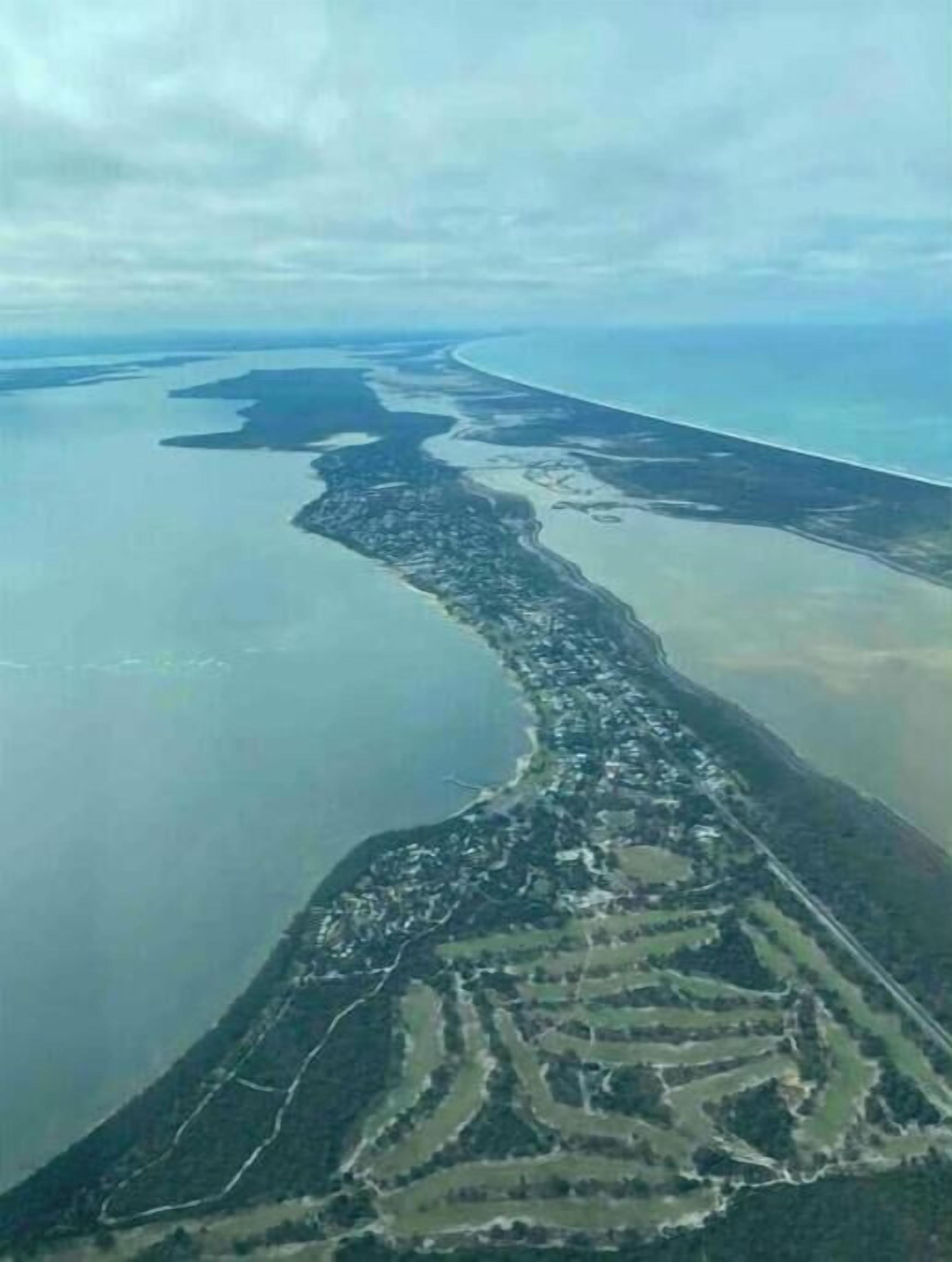 Ett flygbildsbild av ett kustområde med en lång, smal landremsa med byggnader och vägar.