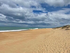 A beach with sand, waves, and a cloudy sky.