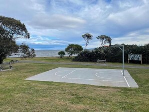 An outdoor basketball court with a bench, trees, and a view of the sea.