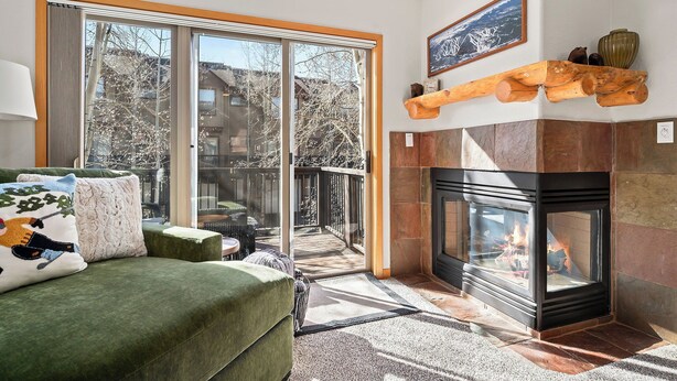 Ein modernes Wohnzimmer mit Kamin, großen Fenstern und einem gemütlichen, grünen Sofa.