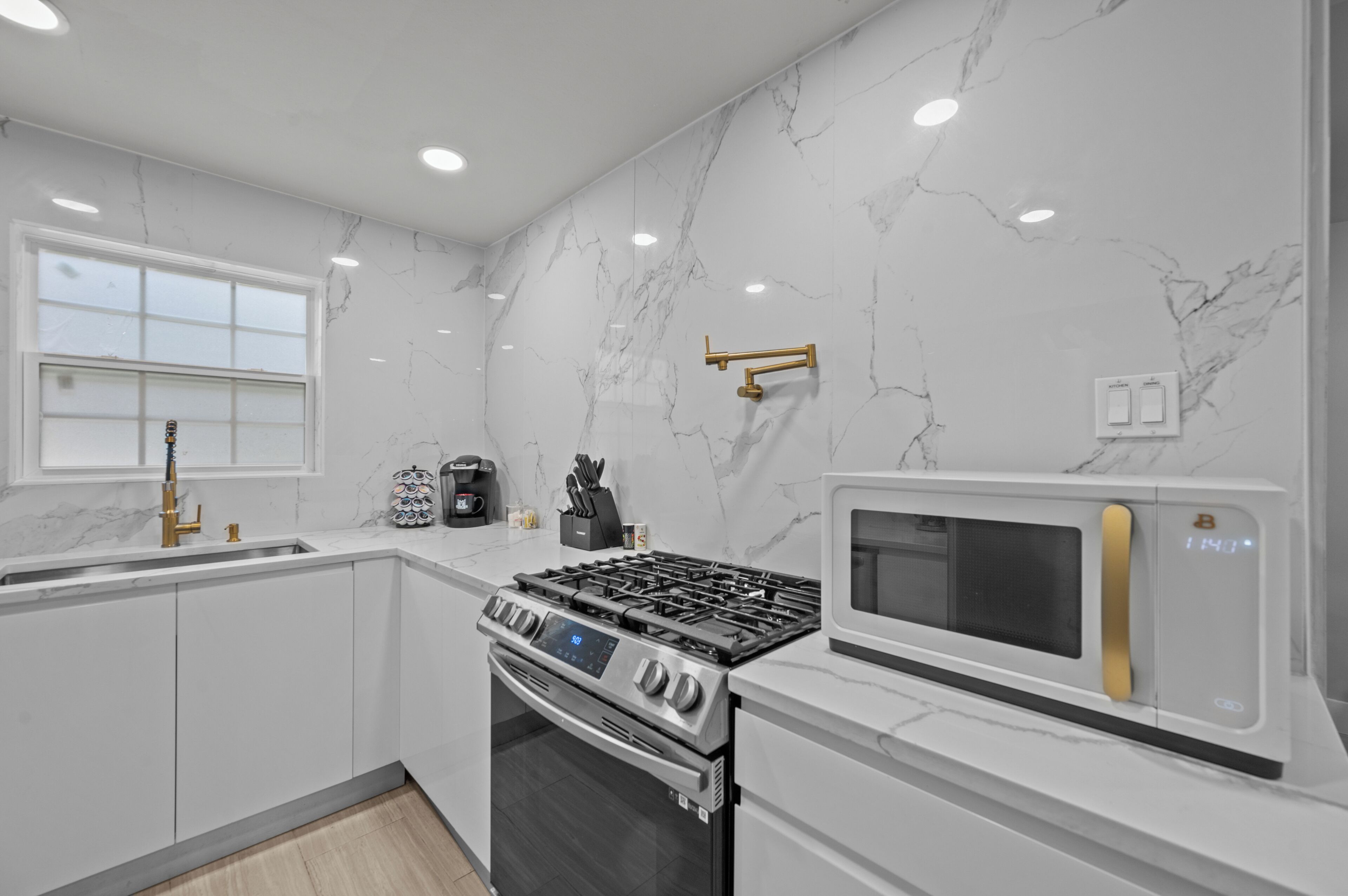 A modern kitchen with white marble walls, stainless steel appliances, and a window.