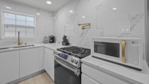 A modern kitchen with white marble walls, stainless steel appliances, and a window.