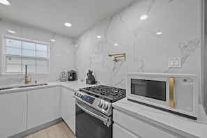 Une cuisine moderne avec des murs en marbre blanc, des appareils électroménagers en acier inoxydable et une fenêtre.