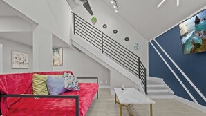 A modern living room with a red sofa, a white coffee table, a staircase, and a wall-mounted TV.