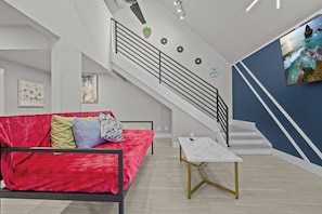 Un salon moderne avec un canapé rouge, une table basse blanche, un escalier et un téléviseur fixé au mur.