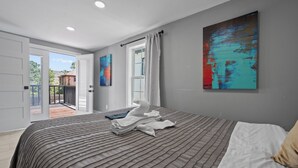 A modern bedroom with a large bed, a view to the outside, and a painting on the wall.