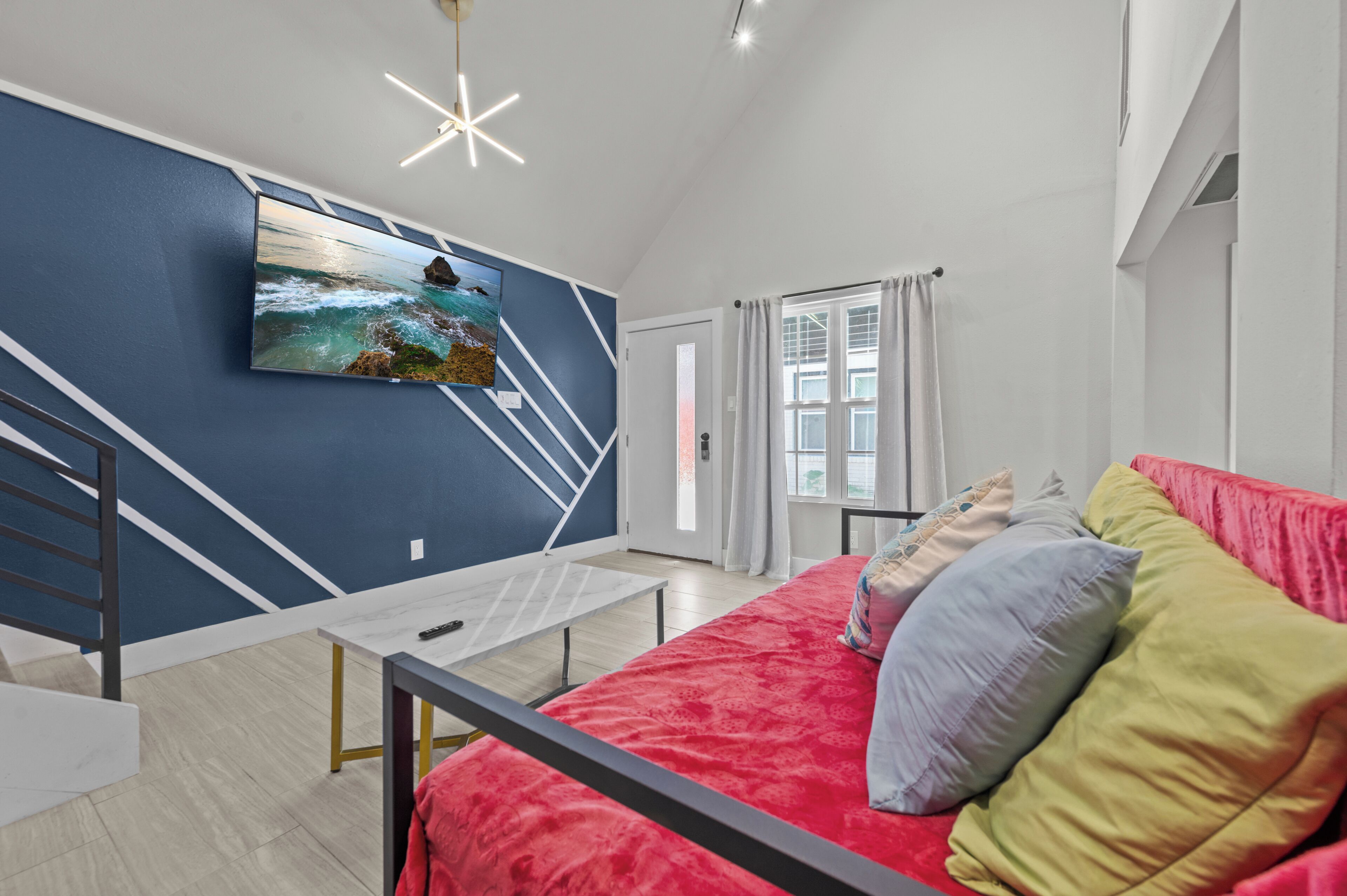 A modern bedroom with a bed, a TV mounted on the wall, a staircase, and a window with curtains.