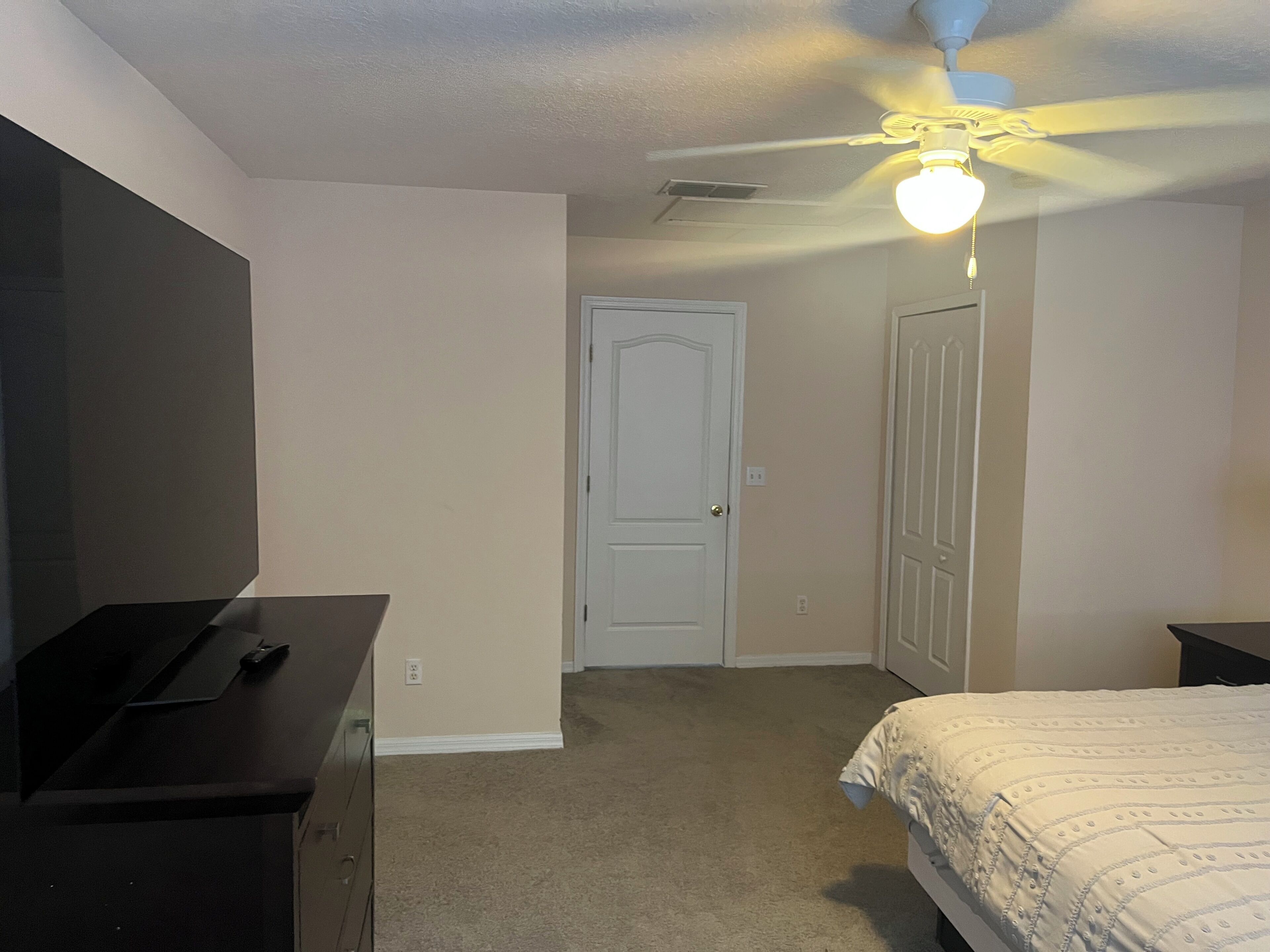 A bedroom with a bed, dresser, ceiling fan, and a door.