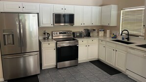 A modern kitchen with stainless steel appliances, white cabinetry, and a black floor mat. - 5bd 4bth 20 min to Disney FREE Heated POOL & Spa. 2 Master suites. (Davenport)