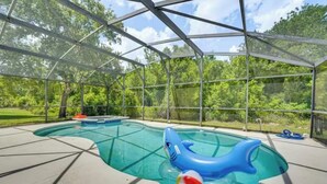 A swimming pool with a shark float, surrounded by a glass enclosure with a view of trees. - 5bd 4bth 20 min to Disney FREE Heated POOL & Spa. 2 Master suites. (Davenport)