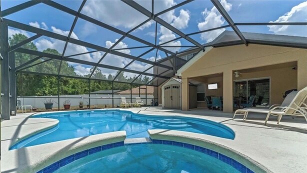 A covered swimming pool with a glass ceiling, lounge chairs, and a building with a beige exterior. - 5bd 4bth 20 min to Disney FREE Heated POOL & Spa. 2 Master suites. (Davenport)