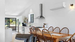 Una cocina moderna con armarios blancos, una campana extractora de acero inoxidable y un comedor con mesa y sillas de madera.
