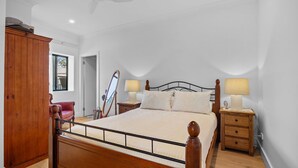 Un dormitorio con estructura de cama de madera, dos mesitas de noche con lámparas, un armario de madera y una silla roja.