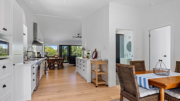 Una cocina moderna con muebles blancos, una zona de comedor con mesa de madera y sillas de mimbre, y vistas al exterior.