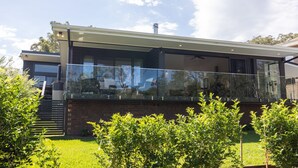 Una casa moderna con balcón de vidrio, paredes de ladrillo y cielo despejado.