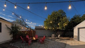 A backyard with stone flooring, a fire pit, red chairs, and string lights. - Sugarhouse Retreat - Walk to Shops + Parks - Cozy Home w/ Private Yard (Salt Lake City)