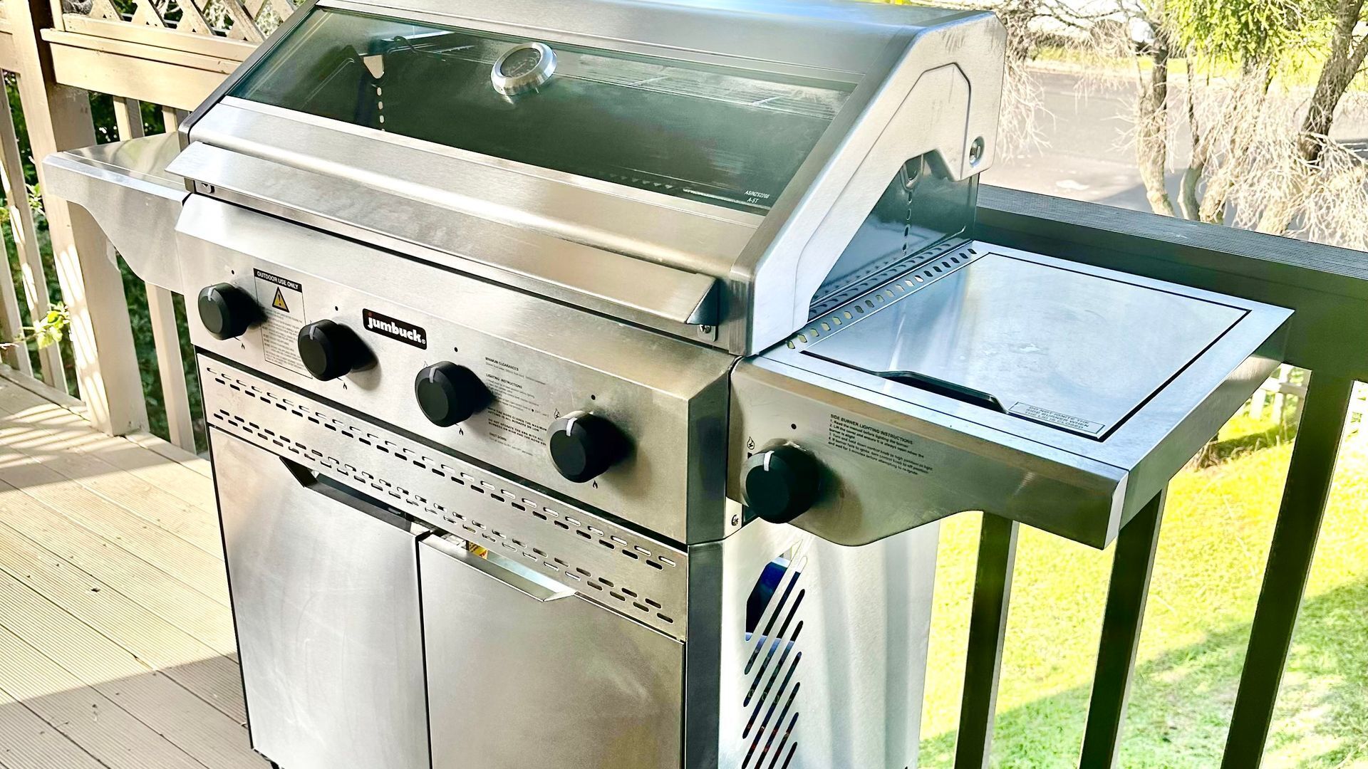 Ein Edelstahl-Grill für den Außenbereich mit vier Brennern, einer Glasabdeckung und einer seitlichen Kochgelegenheit.