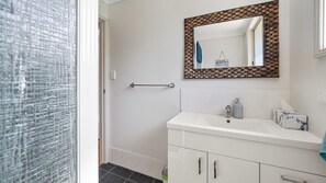 Un bagno con un lavandino bianco, uno specchio con cornice intrecciata, un porta asciugamani e un piccolo cestino.