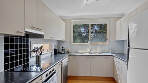 Uma cozinha moderna com armários brancos, bancada preta, janela com vista para árvores e lava-louças.