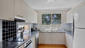 A modern kitchen with white cabinets, a black countertop, a window with a view of trees, and a dishwasher. - Seabreeze Cottage Pet Friendly Family Holiday Home close to the Beach (Manyana)