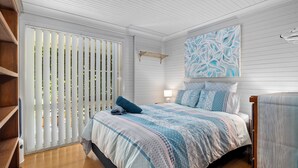 Quarto com cama, mesa de cabeceira, abajur, janela com persianas e uma obra de arte na parede.