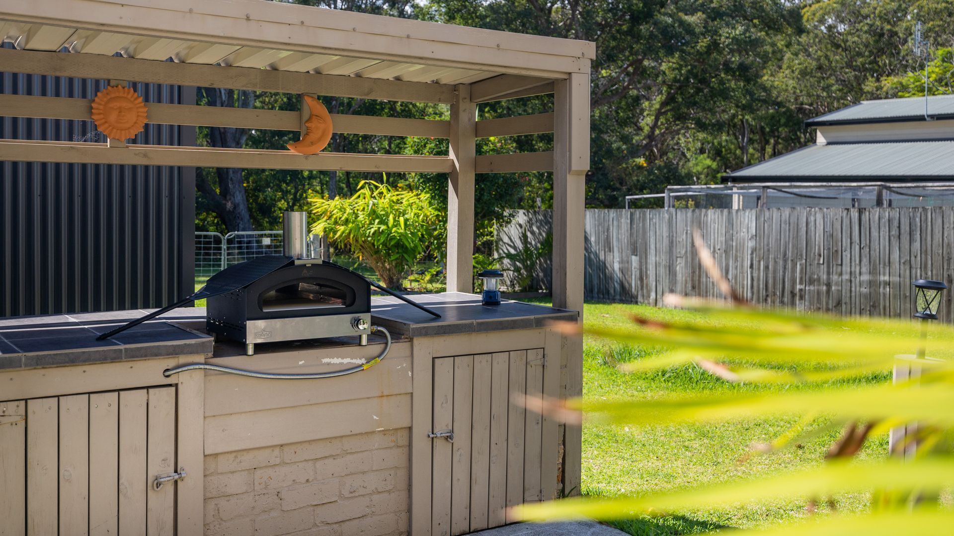 Ein Grill mit Baldachin, eine Hängeleuchte und ein Holzzaun im Hintergrund.