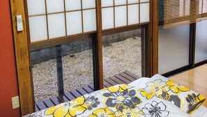 A room with a sliding glass door, a bed with a floral bedspread, and a wooden floor. - Shiki House (Shiki)