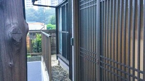 A wooden door with a metal gate, a concrete pathway, and a view of a building and greenery. - Shiki House (Shiki)
