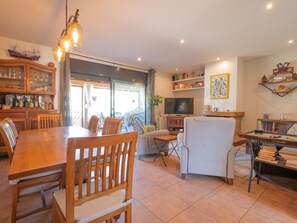 A spacious living area with a dining table, chairs, a TV, and a bookshelf. - Can Jamy by Costabravaway (calonge)