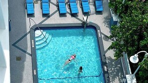 Une piscine où une personne nage, avec un sauveteur et des chaises longues bleues.