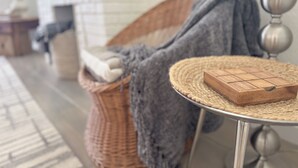 A wicker chair with a blanket, a small wooden box on a woven table, and a brick fireplace in the background. - 253 Upper Chic Boho Retreat NEW RENO (Erie)